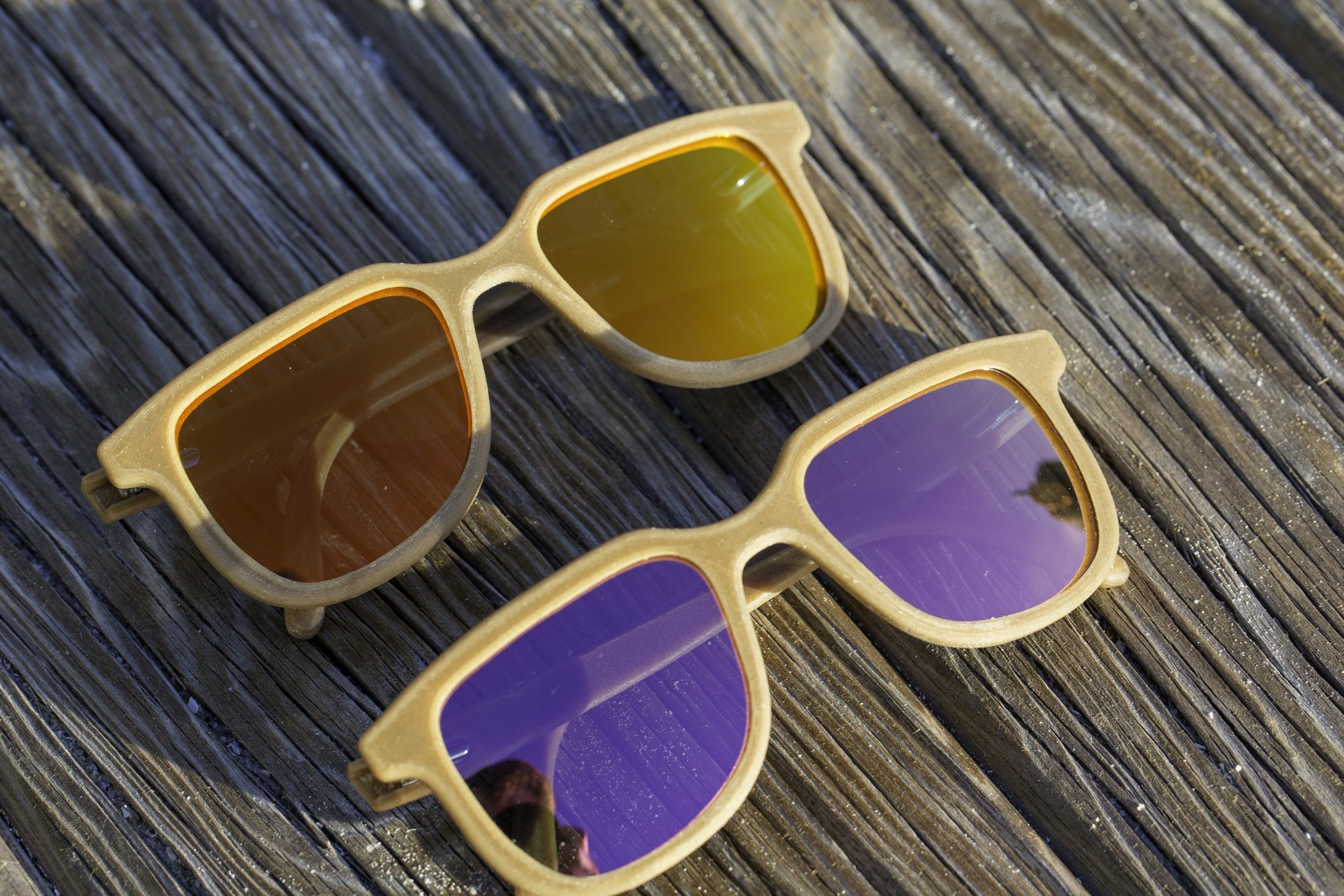 Two pairs of Apollo hemp sunglasses, fire orange and purple mirrored lenses, on weathered wood